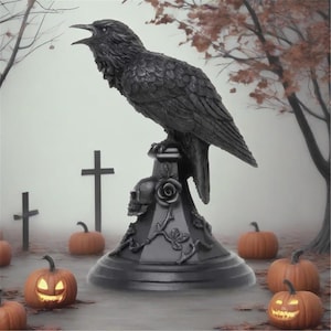 May include: A black raven statue perched on a decorative base featuring a skull and rose design. The raven is surrounded by pumpkins and tombstones, creating a spooky Halloween scene. The pumpkins have carved faces and glowing lights.