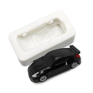 May include: A white silicone mould for making a small black car cake topper. The mould is shaped like a car and has a detailed interior. The cake topper is a black car with a spoiler and black wheels.