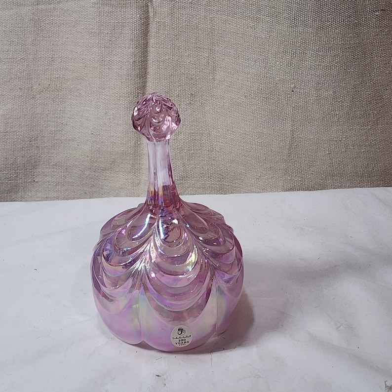 May include: Pink iridescent glass swan shaped dish with a scalloped design. The dish has a sticker on the bottom that reads "100 Years of Glass".