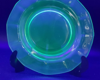 May include: A clear, green glass plate with a scalloped edge. The plate is glowing green under a black light.