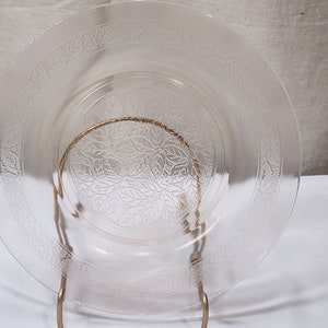 May include: A clear glass plate with a floral pattern. The plate is on a gold metal stand.