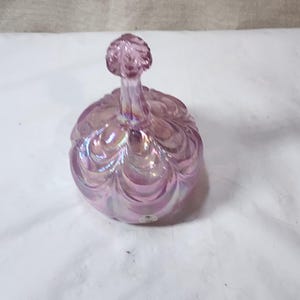 May include: A pink iridescent glass bottle stopper with a swirl design. The stopper has a round, bulbous base and a knob on top.