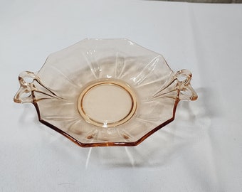 Puede incluir: Un plato para servir de vidrio transparente rosa pálido con dos asas. El plato tiene un borde festoneado y un centro elevado.