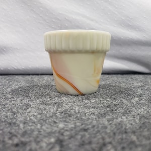 Op de afbeelding: Een kleine witte en oranje marmeren glazen plantenpot met een geribbelde rand.