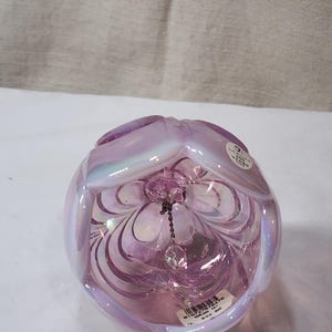 May include: A pink iridescent glass bell with a delicate chain and crystal charm. The bell has a scalloped design and is inscribed with "100 Years of Memories".