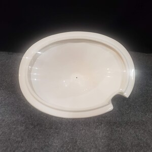 May include: White ceramic lid with a small spout on the side. The lid is round and has a smooth, glossy finish.