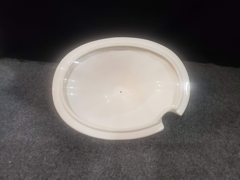 May include: White ceramic lid with a small spout on the side. The lid is round and has a smooth, glossy finish.