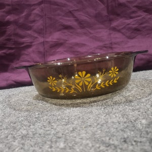 Puede incluir: Un molde para hornear de vidrio marrón con un diseño floral en amarillo. El molde tiene una forma redondeada y dos asas.