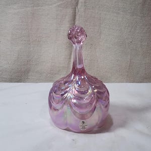 May include: Pink iridescent glass bell with a scalloped design and a knob on top. The bell has a sticker on the bottom that says "75th Anniversary 100 Years 1918-2018".