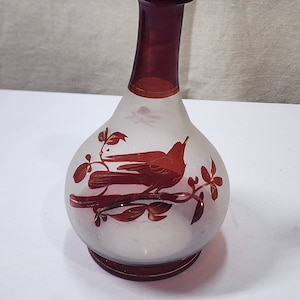 Può includere: Un piccolo vaso di vetro smerigliato con un design di uccello rosso e foglia d'oro. Il vaso ha un collo e una base in vetro rosso.