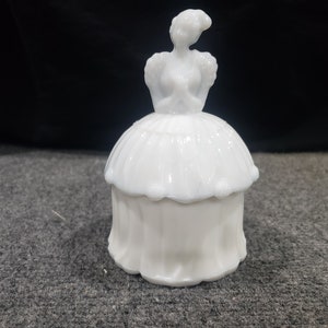 Op de afbeelding: Witte melk glazen sieraden doos met een deksel in de vorm van een vrouw in een jurk.