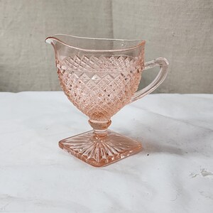 May include: A pink glass creamer with a diamond pattern and a footed base.