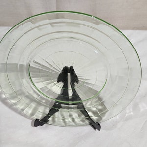 May include: A clear glass plate with a green rim and a concentric circle design. The plate is on a black stand.