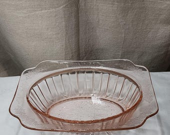 May include: A vintage pink glass serving dish set. The set includes an oval bowl with vertical ridges and a rectangular tray with floral detailing. The glass has a delicate, translucent quality, perfect for serving food.