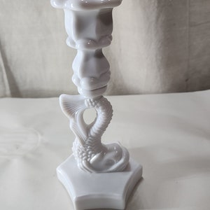 May include: White milk glass candlestick with a floral design on the top and a fish design on the base.