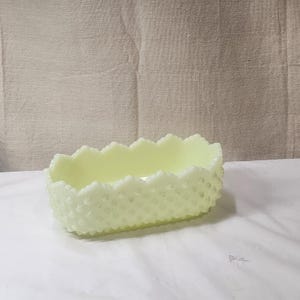 Op de afbeelding: Een lichtgele glazen schaal met een gegolfde rand en een textuur. De schaal is ovaalvormig en heeft een reliëfpatroon van kleine stippen.