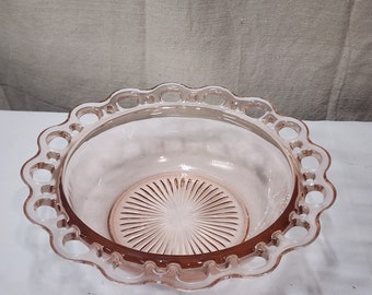 Pode incluir: Uma tigela de vidro rosa com uma borda ondulada com recortes circulares. A tigela tem um design texturizado em forma de estrela na base. A tigela é provavelmente vintage ou antiga e é adequada para servir ou exibir.