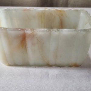 Puede incluir: Un plato rectangular de vidrio marmoleado blanco y marrón con un borde acanalado.