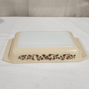 May include: A white ceramic baking dish with a gold floral design around the rim. The dish is empty and has a white interior.