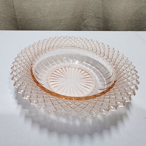 May include: A pink glass bowl with a diamond pattern around the rim and a sunburst pattern on the bottom.