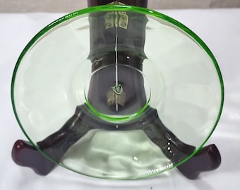 May include: A green glass saucer with a scalloped edge. The saucer is sitting on a wooden stand.