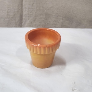 Op de afbeelding: Een kleine keramische bloempot met een geribbelde rand. De pot heeft een kleurovergang, van lichtgeel aan de basis naar warm oranje aan de bovenkant. De binnenkant is ook oranje.