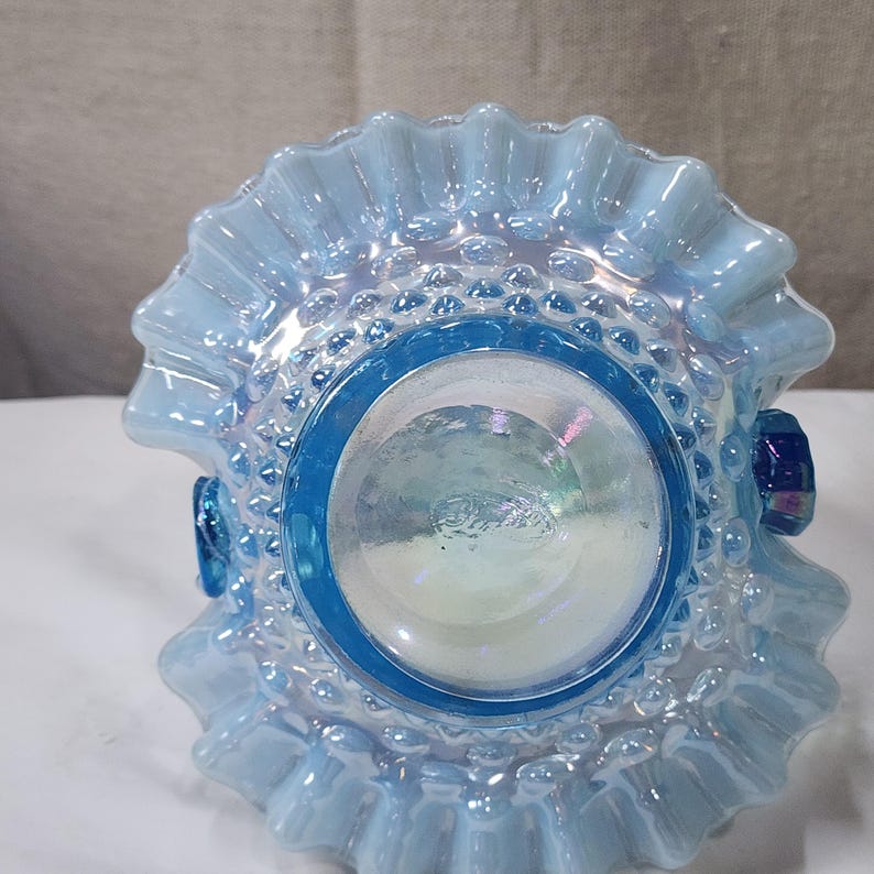 Op de afbeelding: Een blauwe, iriserende glazen kom met een gekrulde rand en een getextureerde bodem. De kom heeft een heldere glazen basis en een blauwe, iriserende bovenkant.