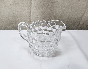 Peut inclure: Une crémier en verre transparent avec un motif en diamant. La crémier a une poignée et un bord festonné.