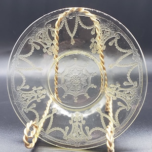 May include: A clear glass saucer with a yellow floral design and a gold metal stand. The saucer has a scalloped edge and a raised center.