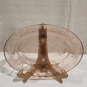 May include: A pink glass plate with a floral design. The plate is on a gold metal stand.