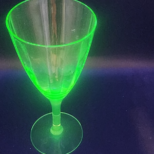 May include: A vintage, clear glass cocktail or wine glass with a bright neon green rim and stem. The glass has a wide, conical bowl and a circular base. The glass is likely made of uranium glass, which glows under UV light.