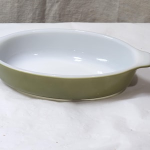Puede incluir: Fuente de horno ovalada de cerámica, con interior blanco y exterior verde oliva. La fuente tiene dos asas pequeñas y es adecuada para hornear y servir. La fuente mide unos 25 cm de largo.