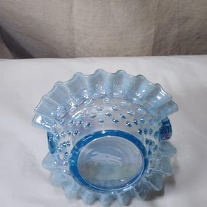 Op de afbeelding: Een blauwe, iriserende glazen kom met een gegolfde rand en een stippenpatroon. De kom is gemaakt van melkglas en heeft een vintage uitstraling.