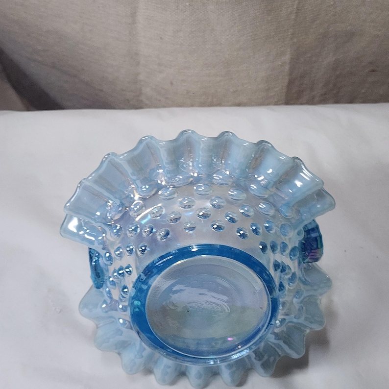 Op de afbeelding: Een blauwe, iriserende glazen kom met een gegolfde rand en een stippenpatroon. De kom is gemaakt van melkglas en heeft een vintage uitstraling.