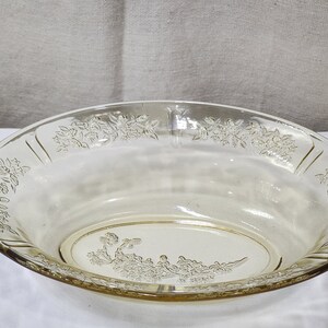 May include: A clear, oval glass serving bowl with a floral design. The bowl has a pale yellow tint and a decorative floral pattern around the rim and in the centre. The bowl is likely vintage or antique.