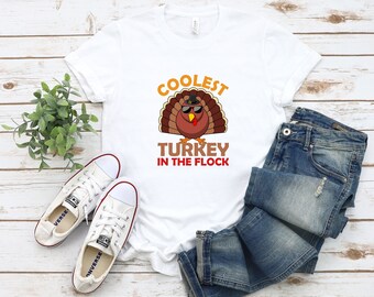 May include: White t-shirt featuring a graphic of a turkey wearing sunglasses and a pilgrim hat. The text "Coolest Turkey in the Flock" is printed below the turkey.