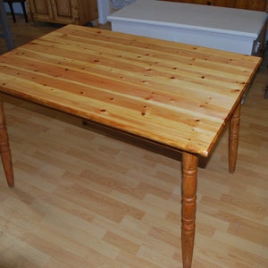 Könnte beinhalten: Ein heller Holztisch mit rechteckiger Tischplatte und gedrehten Beinen. Der Tisch ist aus Naturholz mit einer hellbraunen Oberfläche.