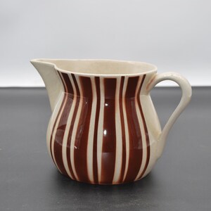 May include: A white ceramic pitcher with brown vertical stripes. The pitcher has a rounded body and a handle.
