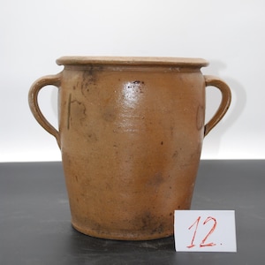 Op de afbeelding: Een bruine keramische pot met twee handvatten. De pot heeft een brede opening en een licht taps toelopend lichaam. Een kleine witte kaart met het nummer "12" staat in de rechter benedenhoek.