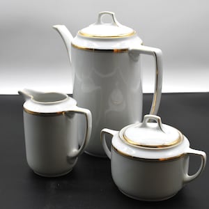 May include: A white porcelain tea set with gold trim. The set includes a teapot, creamer, and sugar bowl.