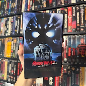 May include: A VHS tape for the movie Friday the 13th Part VI: Jason Lives. The cover features a close-up of Jason Voorhees' hockey mask with the text "Jason Lives" and "Friday the 13th Part VI" below it. The tagline "Kill or Be Killed" is also visible.