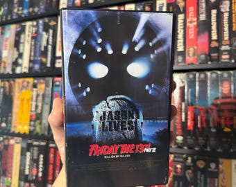 May include: A VHS tape for the film Friday the 13th Part VI: Jason Lives. The cover features a close-up of Jason Voorhees' hockey mask with the text "Jason Lives" and "Friday the 13th Part VI" below it. The tagline "Kill or Be Killed" is also visible.