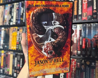 Può includere: Una custodia per videocassetta VHS per il film horror "Jason Goes to Hell: The Final Friday". La custodia presenta un primo piano della maschera da hockey di Jason con una creatura a forma di verme al suo interno. Lo sfondo è di colore arancione e rosso fuoco.
