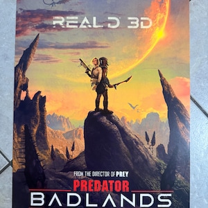 May include: A movie poster for "Predator: Badlands" in theaters November 7. The poster features a figure with a weapon standing on a rocky peak, with a fiery planet and a dragon-like creature in the background. The words "REAL D 3D" are at the top.