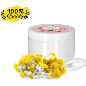 Puede incluir: Un tarro de crema blanco con una etiqueta rosa, junto a un pequeño montón de flores amarillas y una mancha de crema. La etiqueta dice "Immortelle Divine Cream". Una pancarta amarilla con el texto "100% Quality" está en la esquina superior izquierda.