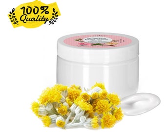 May include: A white jar of cream with a pink label, next to a small pile of yellow flowers and a smear of cream. The label reads "Immortelle Divine Cream". A yellow banner with the text "100% Quality" is in the upper left corner.