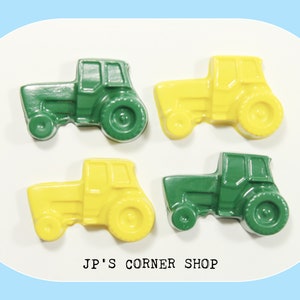May include: Four toy tractors, two green and two yellow, are arranged in a square pattern on a white surface. The tractors have black wheels and are made of plastic.