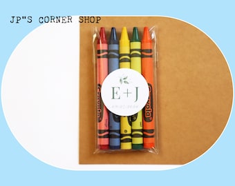 Puede incluir: Un conjunto de cinco lápices de colores en una bolsa de plástico transparente con una pegatina circular blanca que dice "E + J" con un pequeño diseño de hoja verde. Los lápices son rojo, azul, amarillo, verde y naranja.