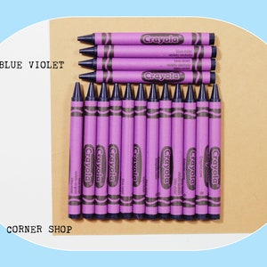 May include: A pack of 12 Crayola crayons in the color Blue Violet. The crayons are arranged in a row on a brown surface. The text "Crayola" is printed on each crayon.