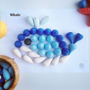 May include: A blue and white whale made from wooden pegs. The whale is on a white background with the word "Whale" written above it.